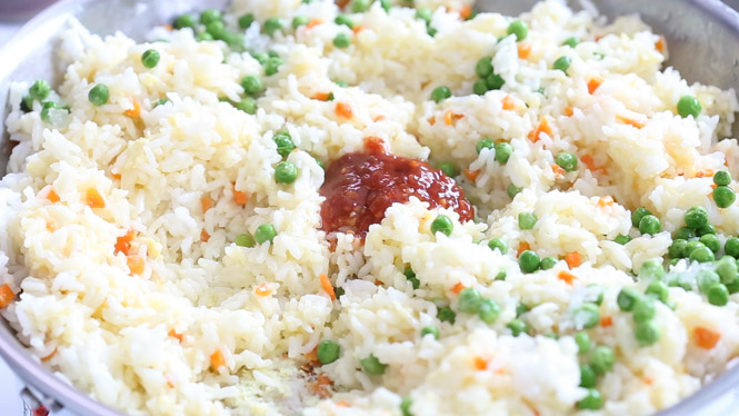 Adding sweet chili sauce to rice and veggies in the skillet.